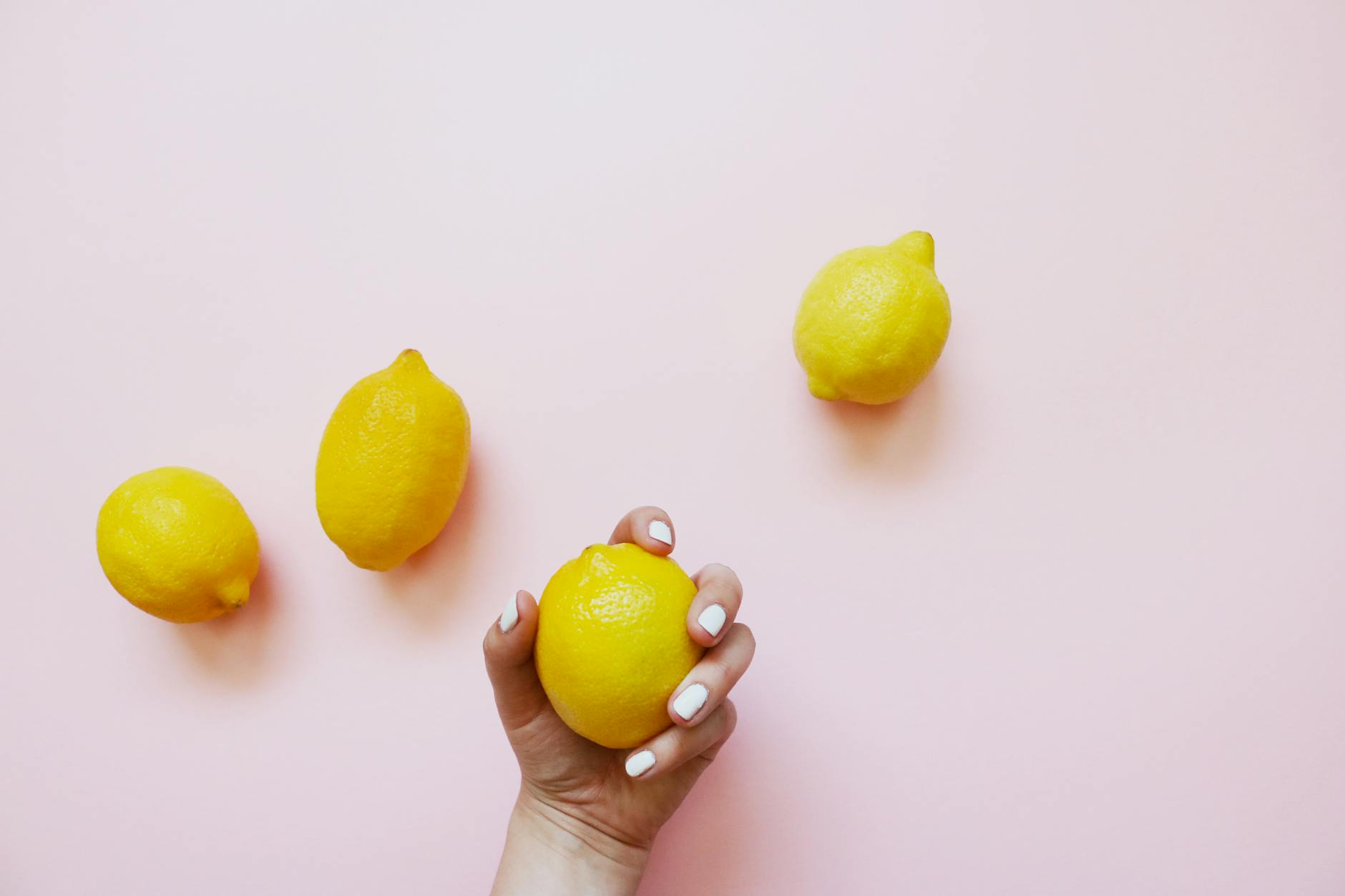 Hand holding a lemon against soft pink background, symbolizing natural pleasure and intimacy