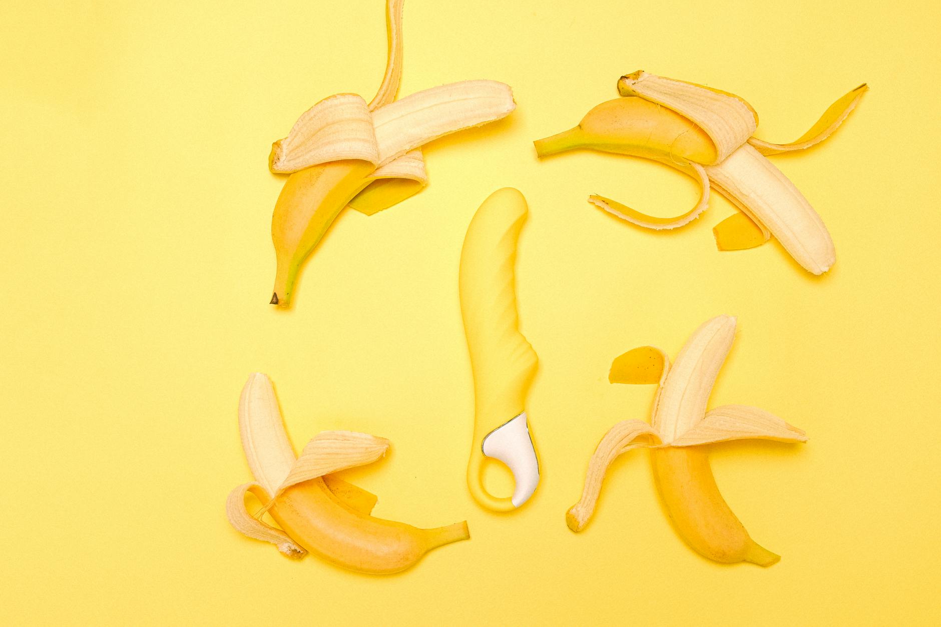 A bright yellow silicone lemon vibrator surrounded by peeled lemons on a sunny yellow surface.