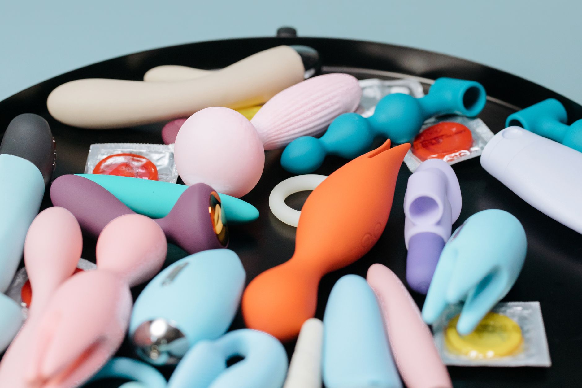 A vibrant collection of various clitoral vibrators and adult toys on a black tray, featuring diverse shapes and colors