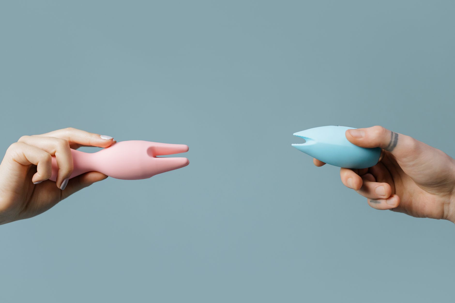 Hands holding colorful silicone vibrators against a pastel background, representing solo and partnered pleasure options.