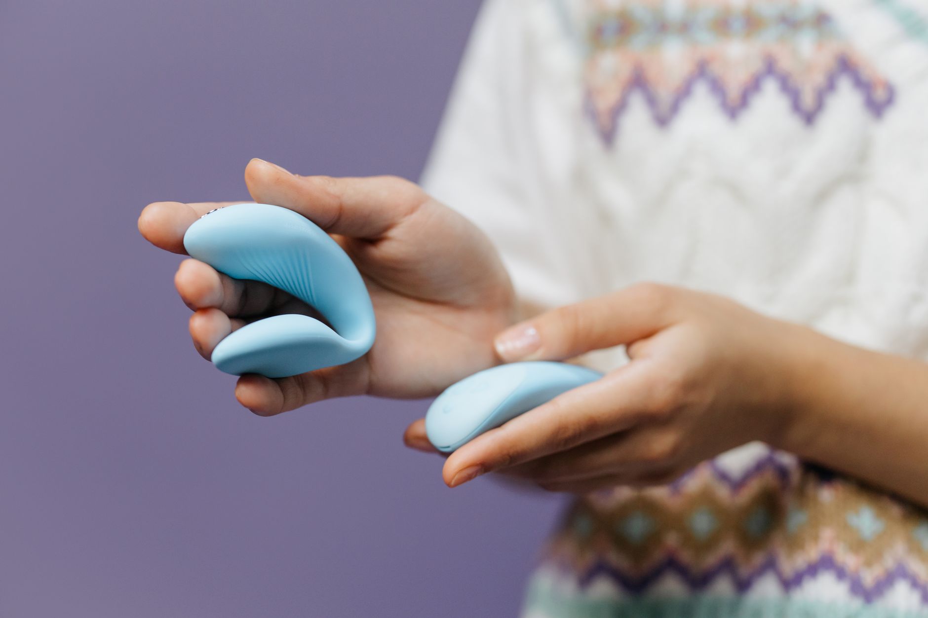 Close-up of hands holding a sleek blue vibrator against a purple background, representing clitoral pleasure restoration.