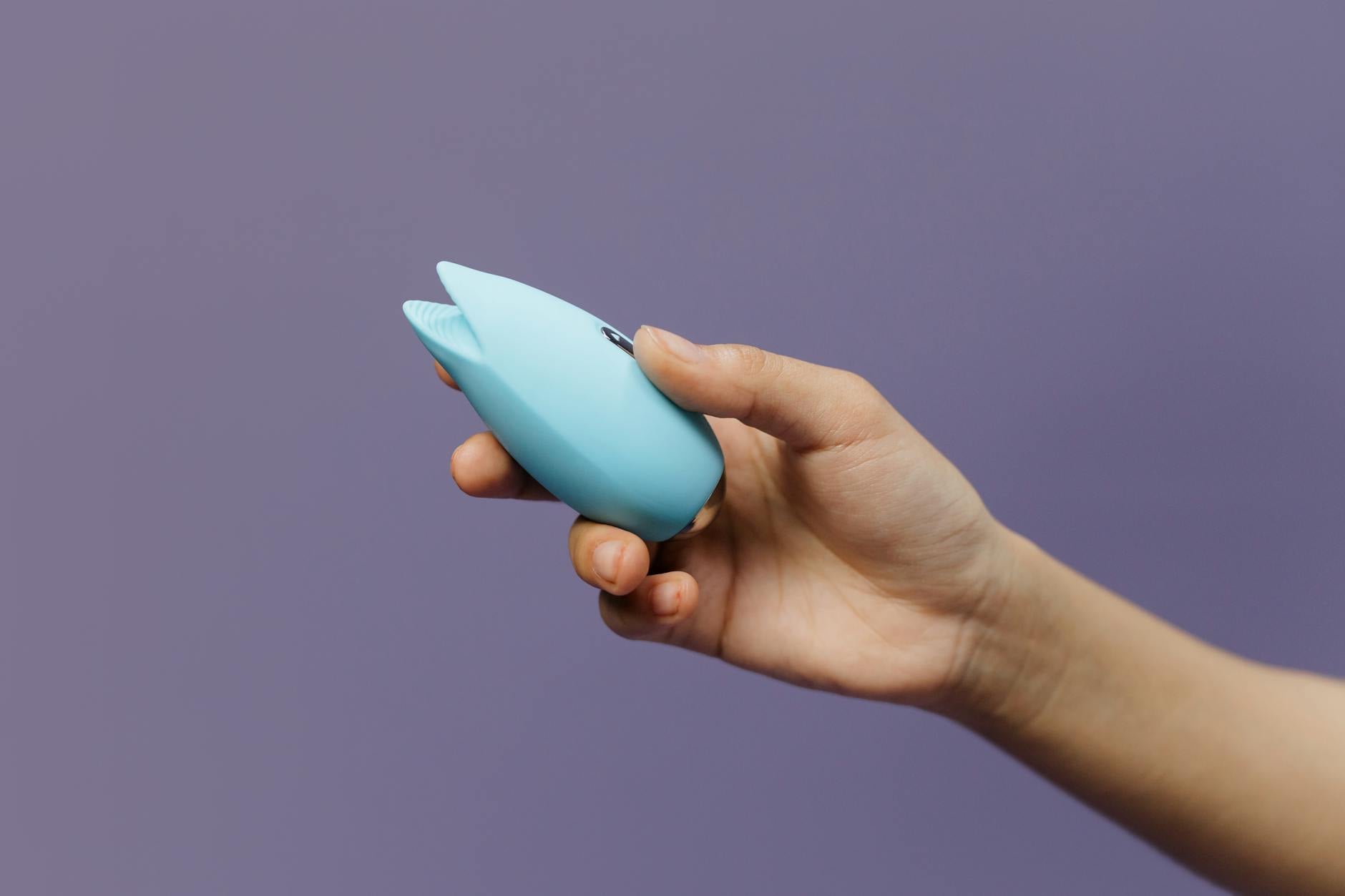 A blue silicone clitoral vibrator held in hand, representing accessible pleasure and pain-free intimacy