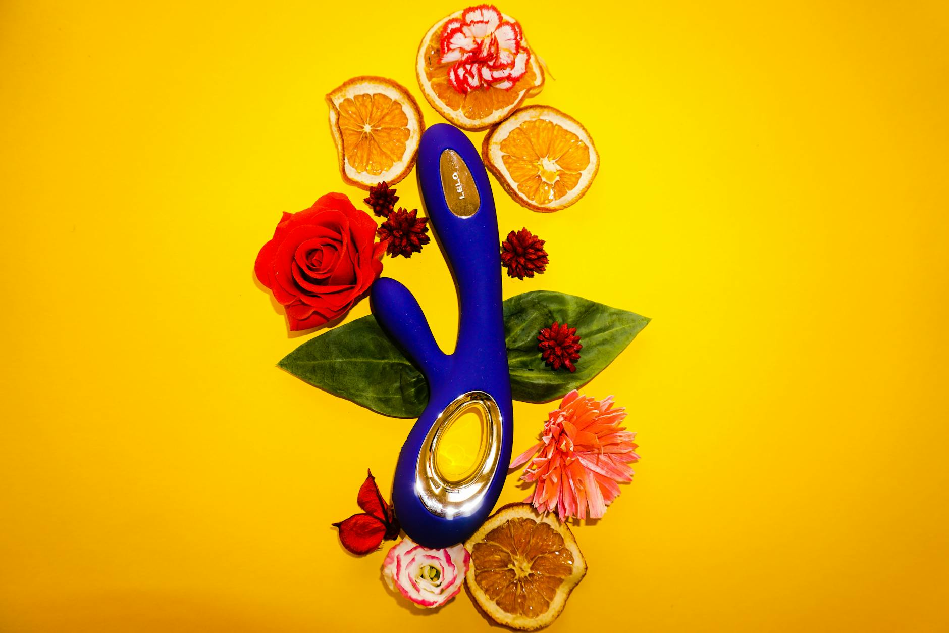 Blue clitoral vibrator surrounded by fresh lemons and flowers on yellow background