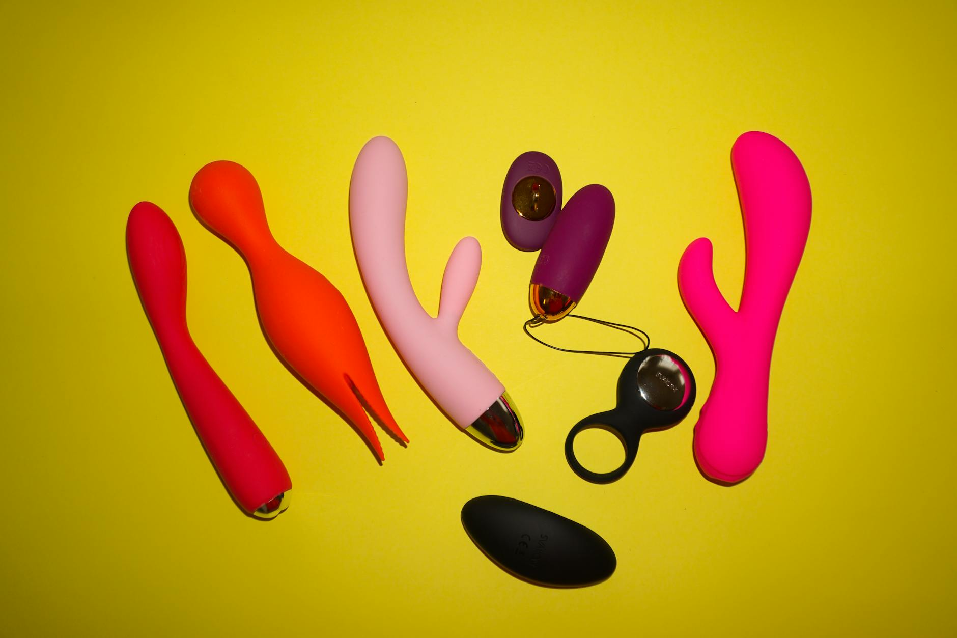 Colorful clitoral vibrators and sex toys arranged on a bright yellow background